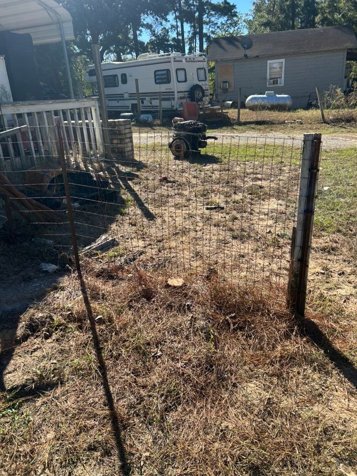 Wire fence gate in front of a rural home, with a motorhome and other buildings in the background.
