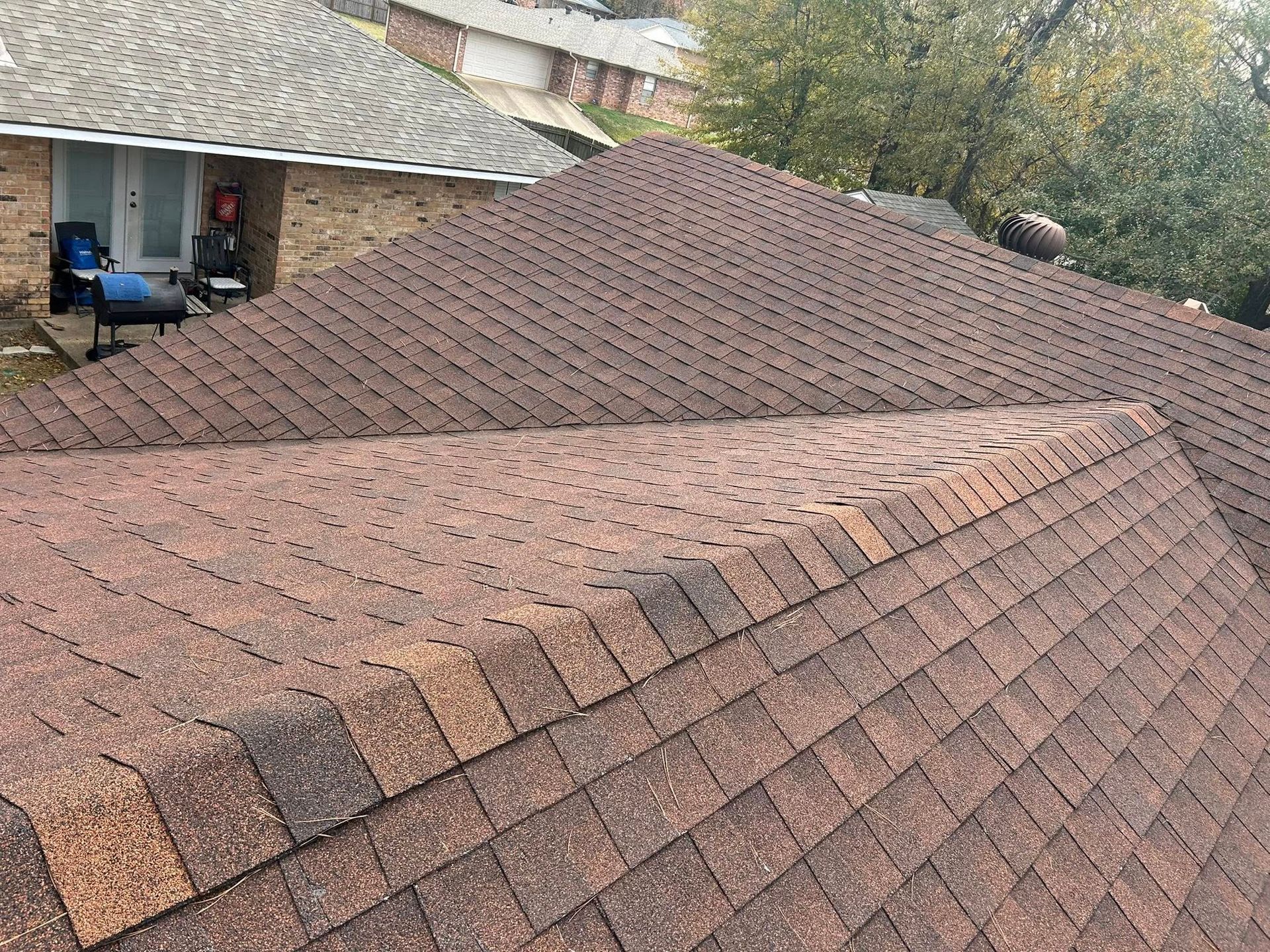 Brown asphalt shingle roof on a house, with a visible ridge line and slight angle to the camera.