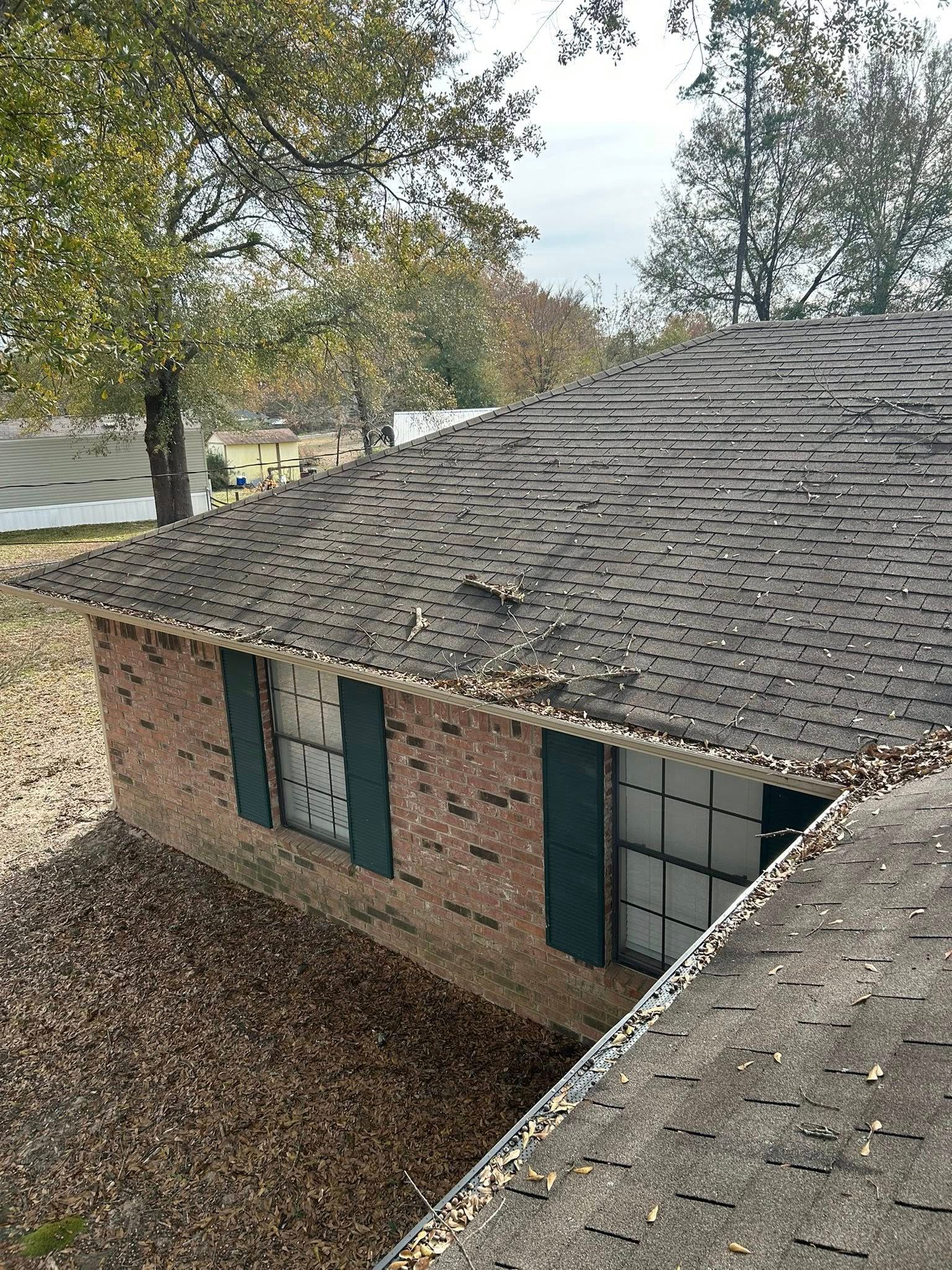 Brick house with damaged roof and boarded-up windows, covered in fallen leaves, under a cloudy sky.