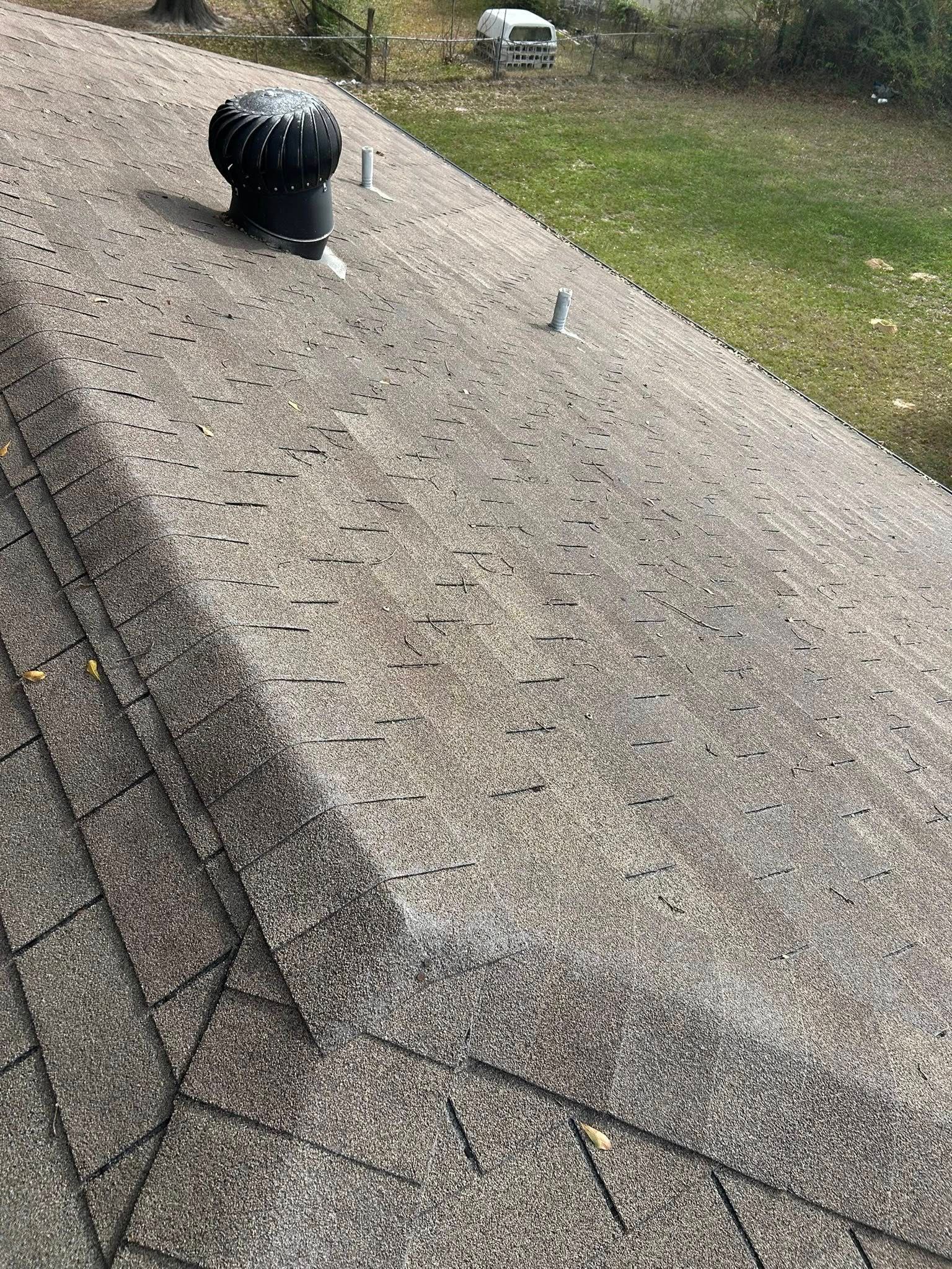 Roof covered with gray asphalt shingles; a black vent, and small metal fasteners are visible.