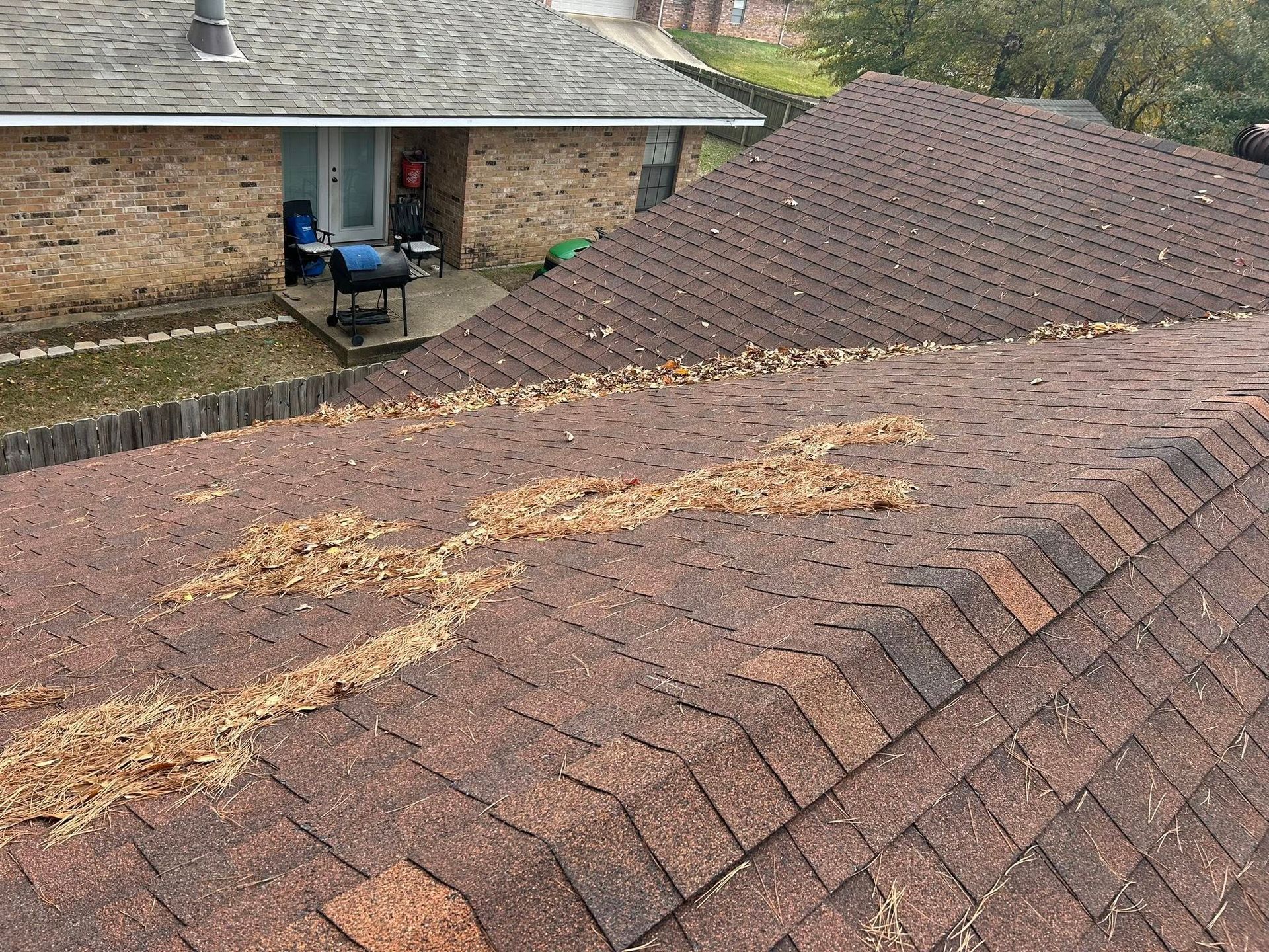 Brown asphalt shingle roof covered in debris. A second house is visible in the background.