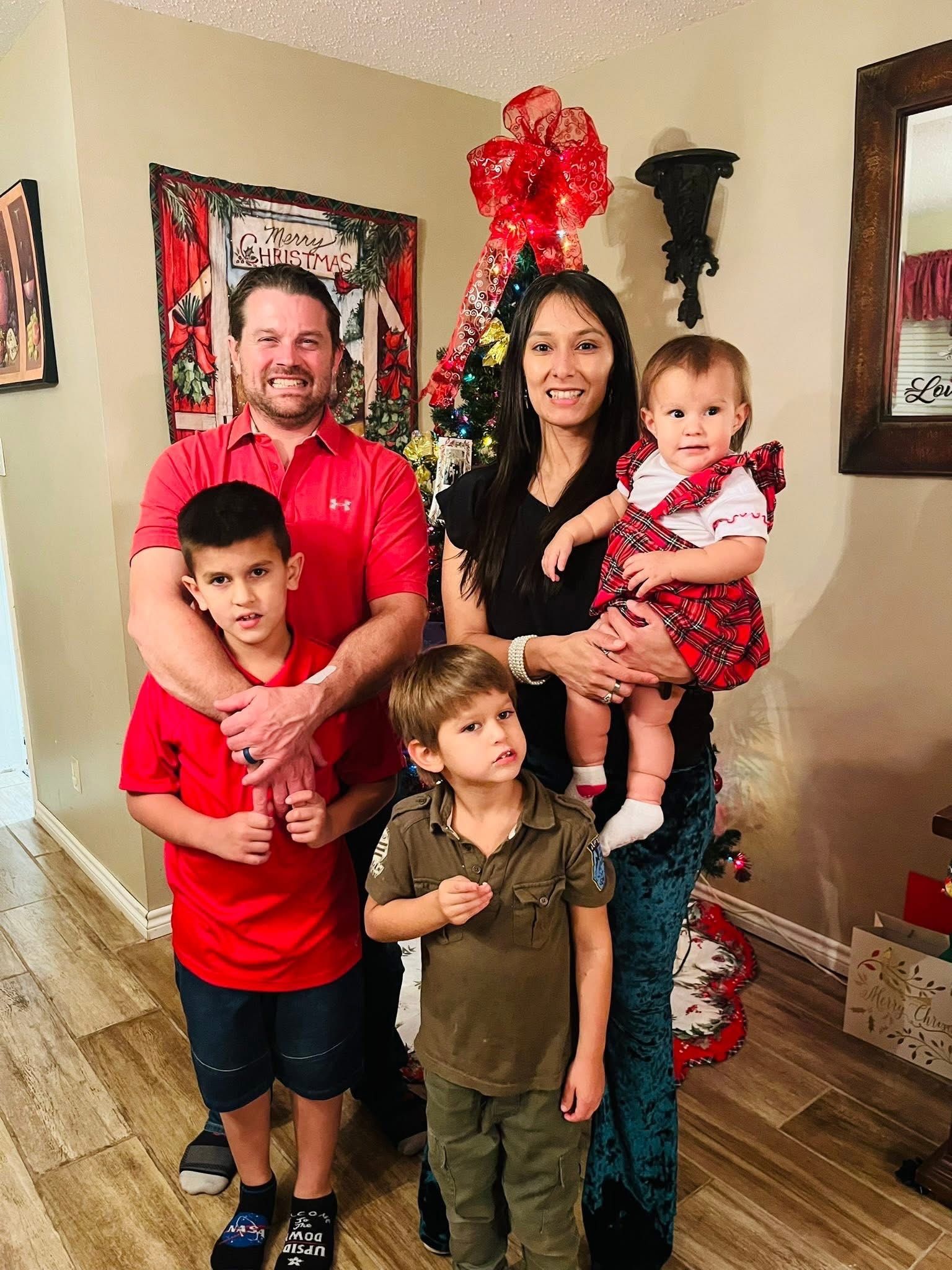 Family of five poses by a Christmas tree; red shirts and dresses; smiling.