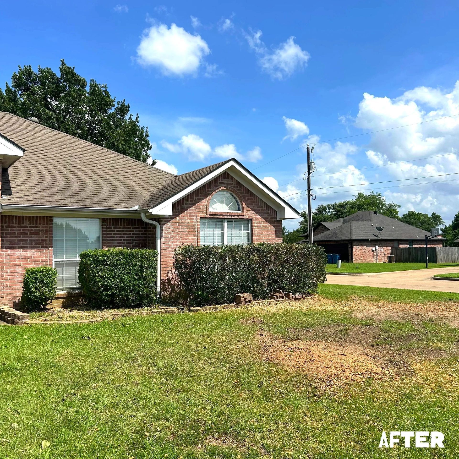 A house with a brick facade and manicured bushes under a blue sky, 