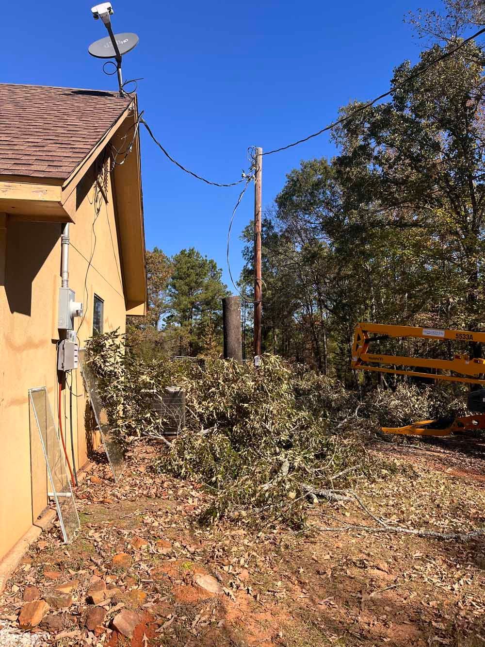 A house with power lines and a utility pole, surrounded by trimmed bushes and clear blue sky.