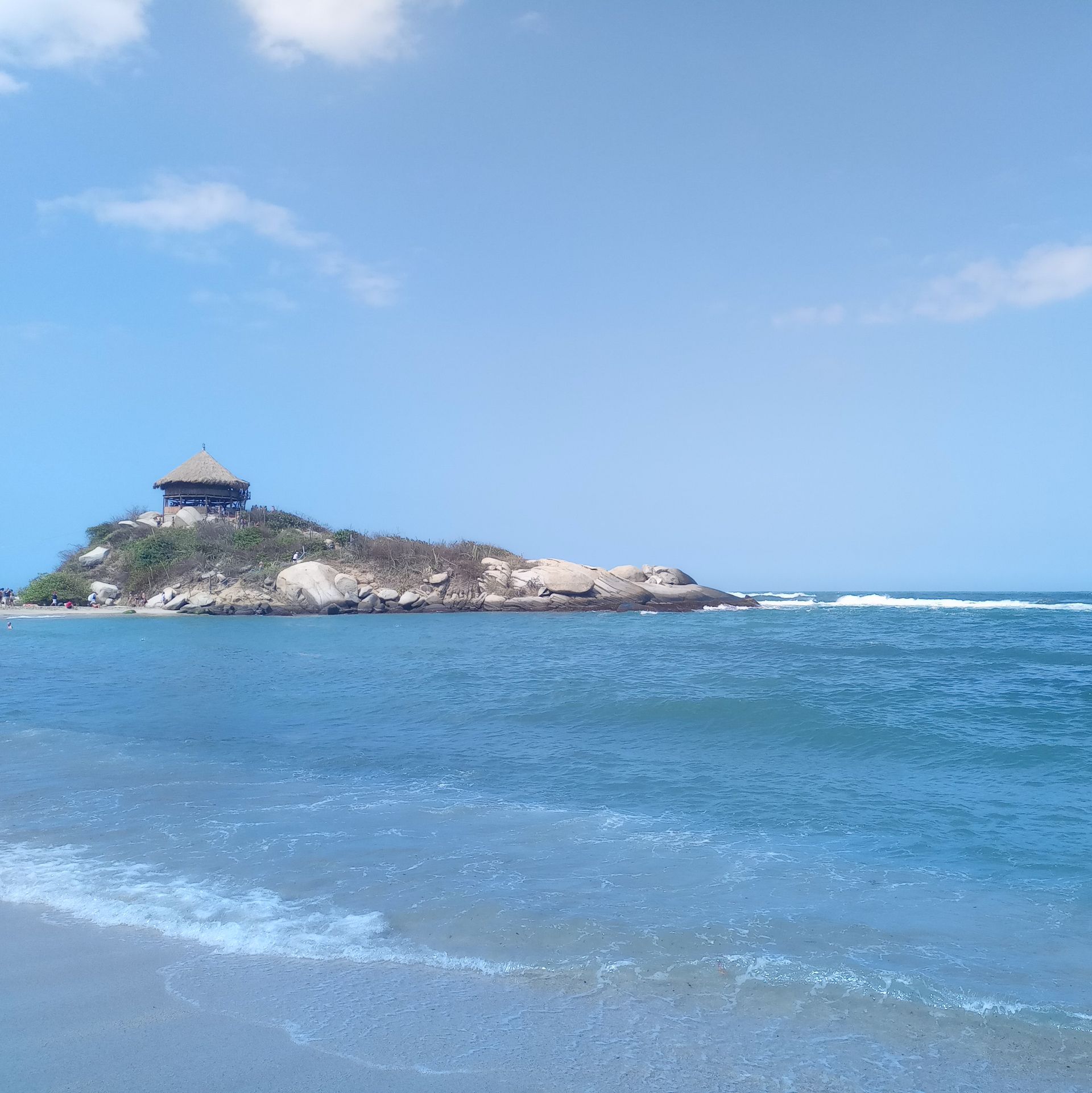 Una escena de playa con una pequeña isla coronada por un mirador. El océano azul se une a la arena bajo un cielo azul brillante.