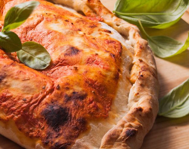 Primo piano di una pizza dorata cotta al forno con foglie di basilico su una superficie di legno.