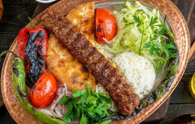 Spiedini grigliati, riso, pomodori e verdure serviti in una ciotola con un peperone bruciacchiato e un ingrediente fritto