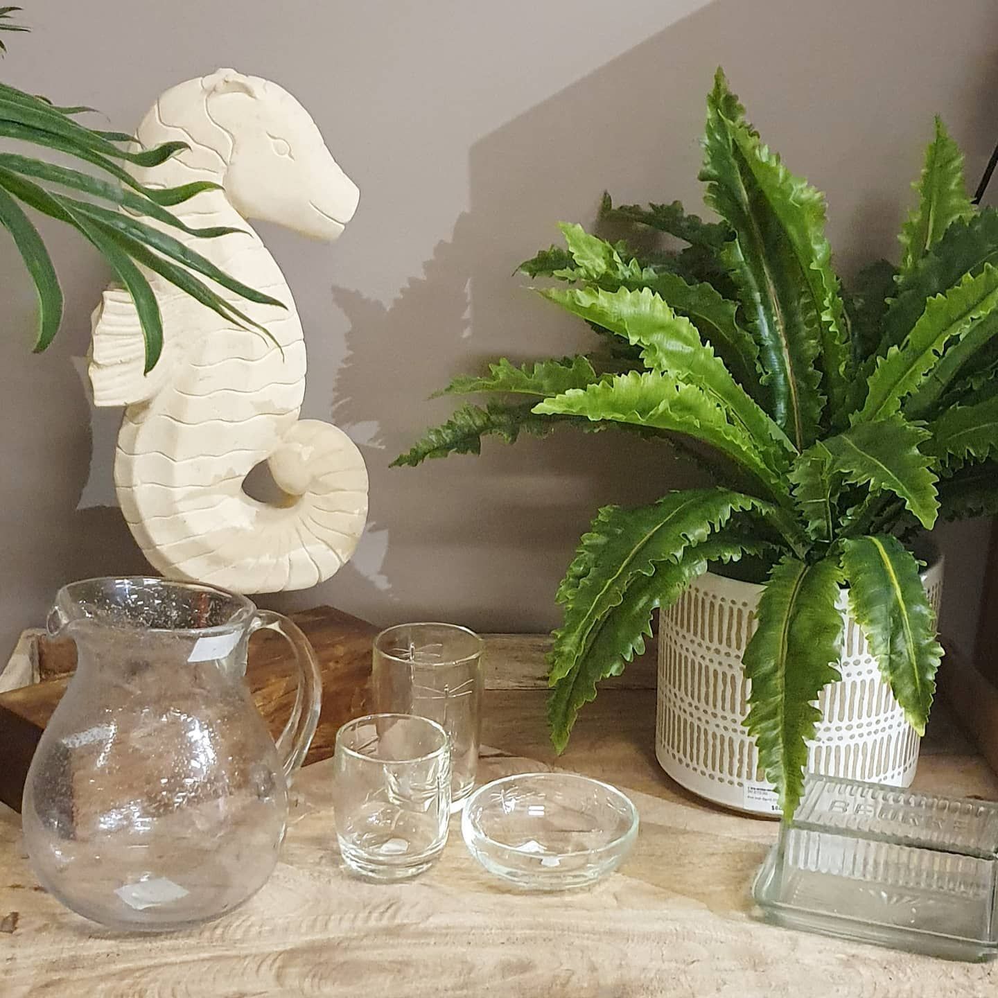 Glass Pitchers and Candles on a Wooden Table Beside a White Seahorse Statue and a Potted Fern — Tropic Living in Trinity Park, QLD