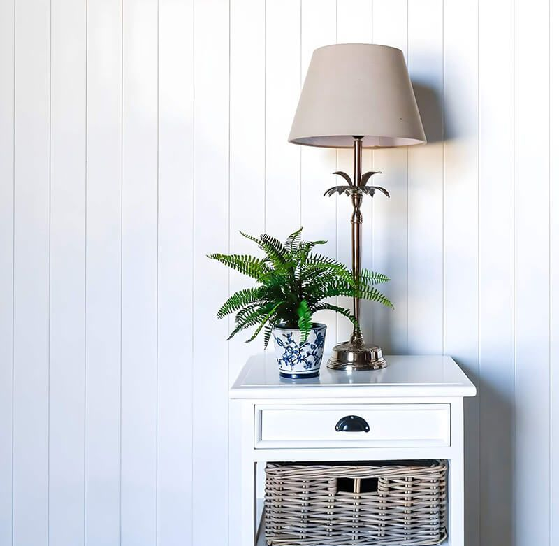 White Nightstand With Lamp, Plant, and Woven Baskets Against a White Paneled Wall — Tropic Living in Smithfield, QLD