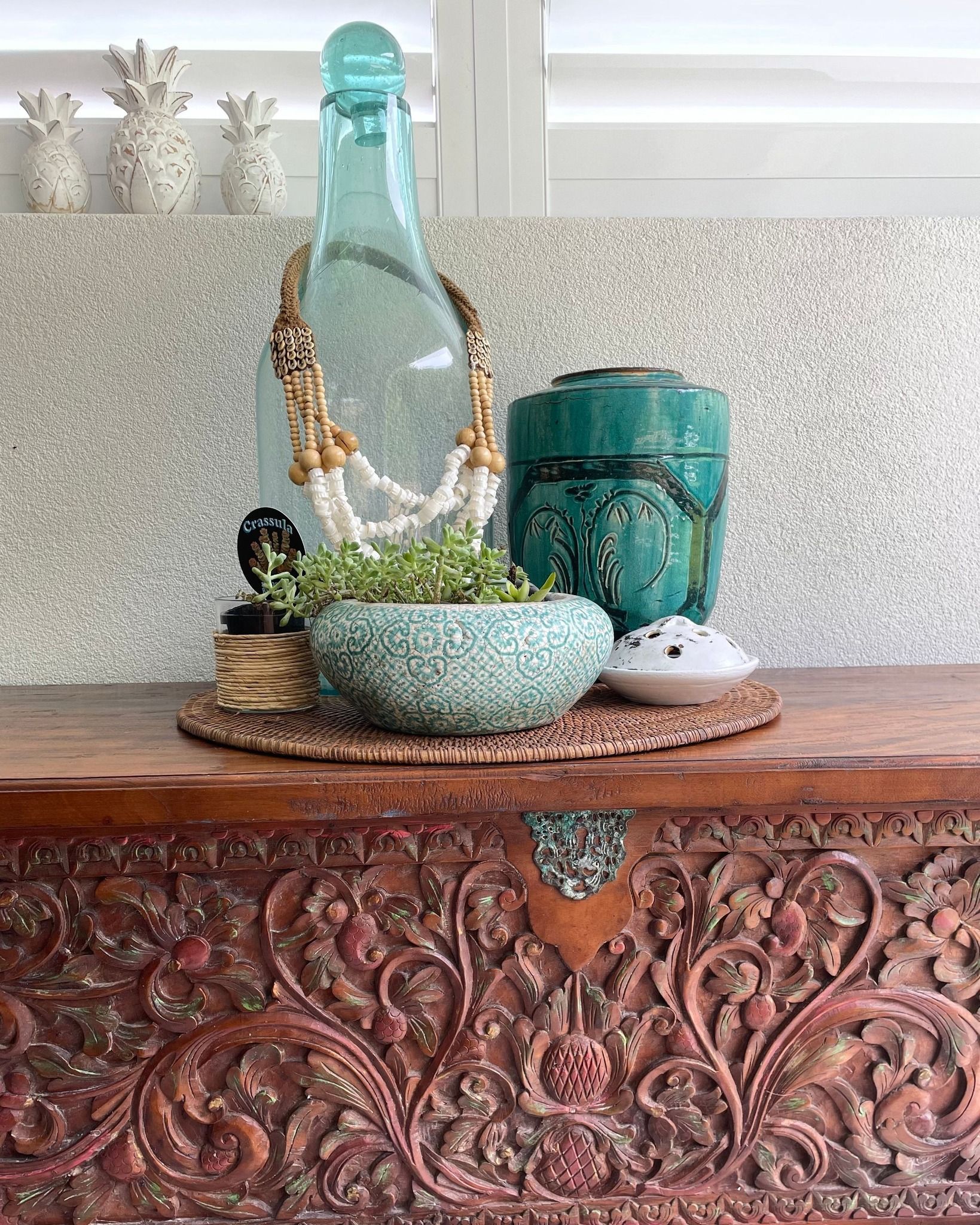 Decorative Glass Bottles and Woven Bowls on a Carved Wooden Chest Against a Textured Wall — Tropic Living in Clifton Beach, QLD