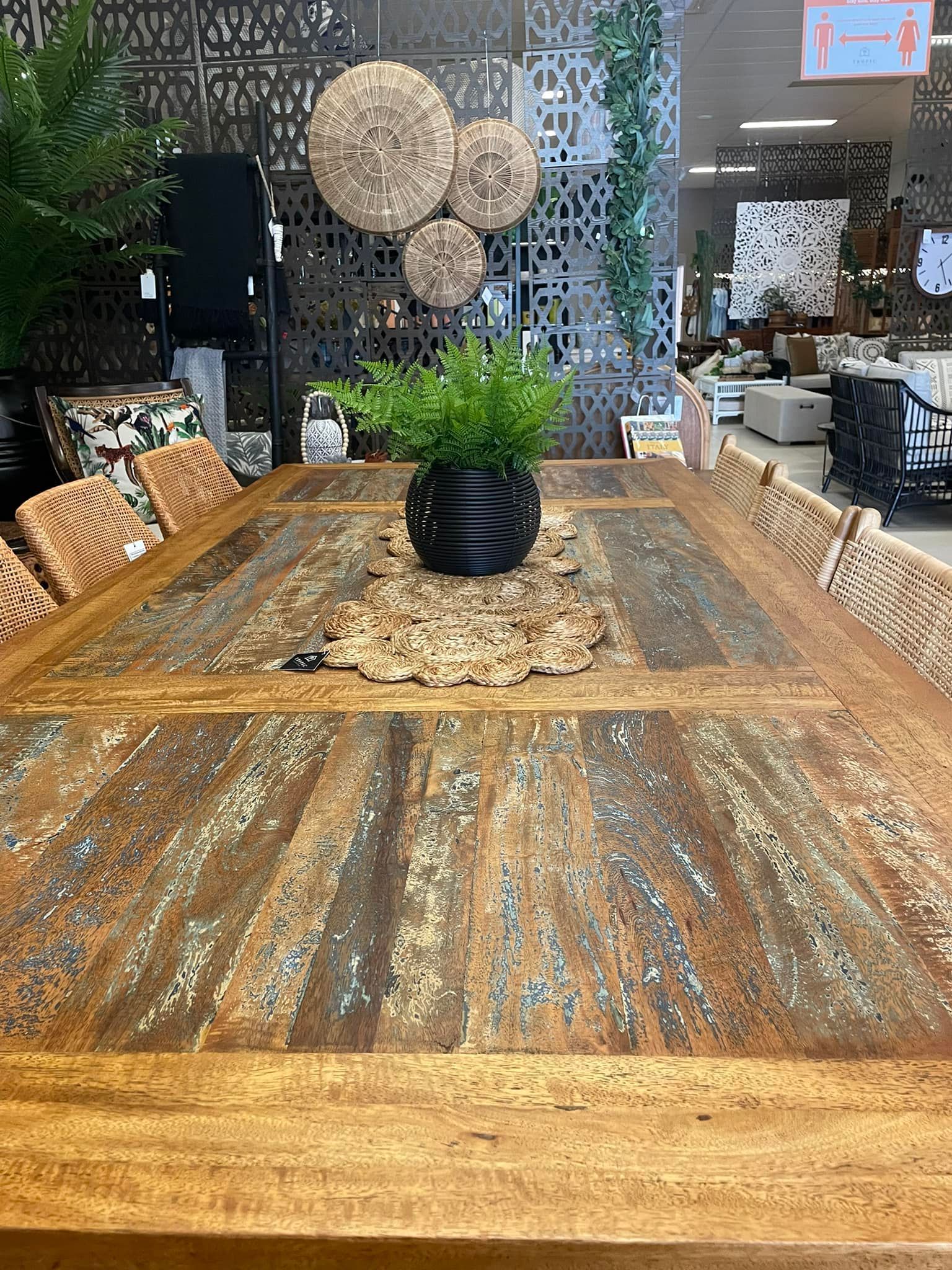 Rustic Wooden Dining Table With Woven Placemats, Black Vase of Greenery, and Rattan Chairs in a Cozy Room — Tropic Living in Mossman, QLD