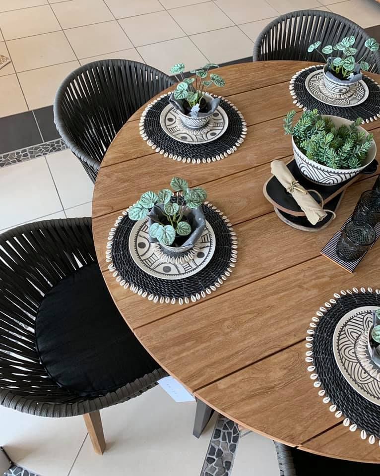 Round Wooden Dining Table With Black Chairs and Small Potted Plants on Decorative Placemats — Tropic Living in Port Douglas, QLD