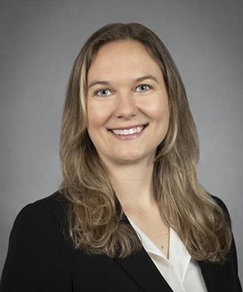 Smiling professional in black blazer and white blouse against a gray background