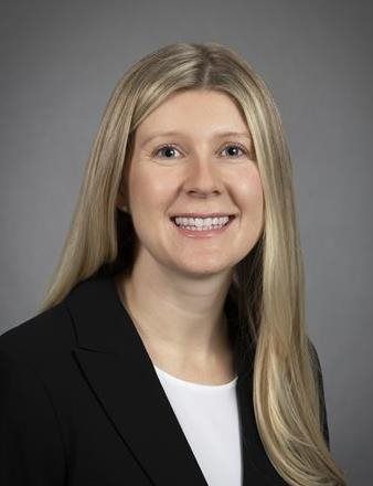 Portrait of a smiling person in a black blazer against a gray studio background