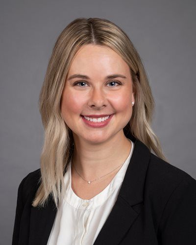 Smiling professional in a black blazer and white blouse against a gray studio background
