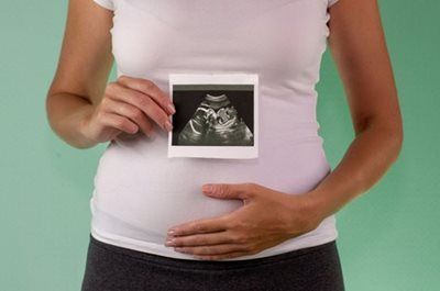 Pregnant person holding ultrasound photo over belly on a green background