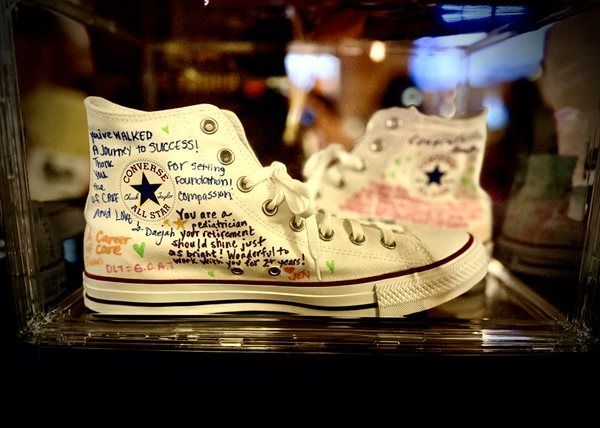 White Converse sneakers covered in handwritten notes, displayed in a glass case