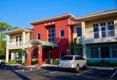 Colorful commercial building with red and beige facades, palm trees, and parked cars on a sunny day