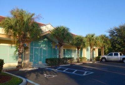 Sunlit office building with palm trees, large windows, and a parking lot with a white truck