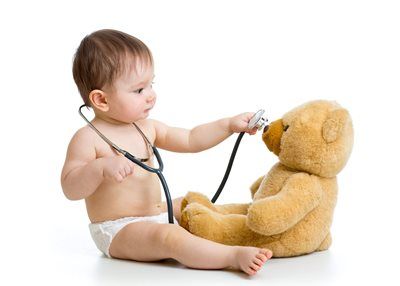 Baby with stethoscope examining a teddy bear on a white background