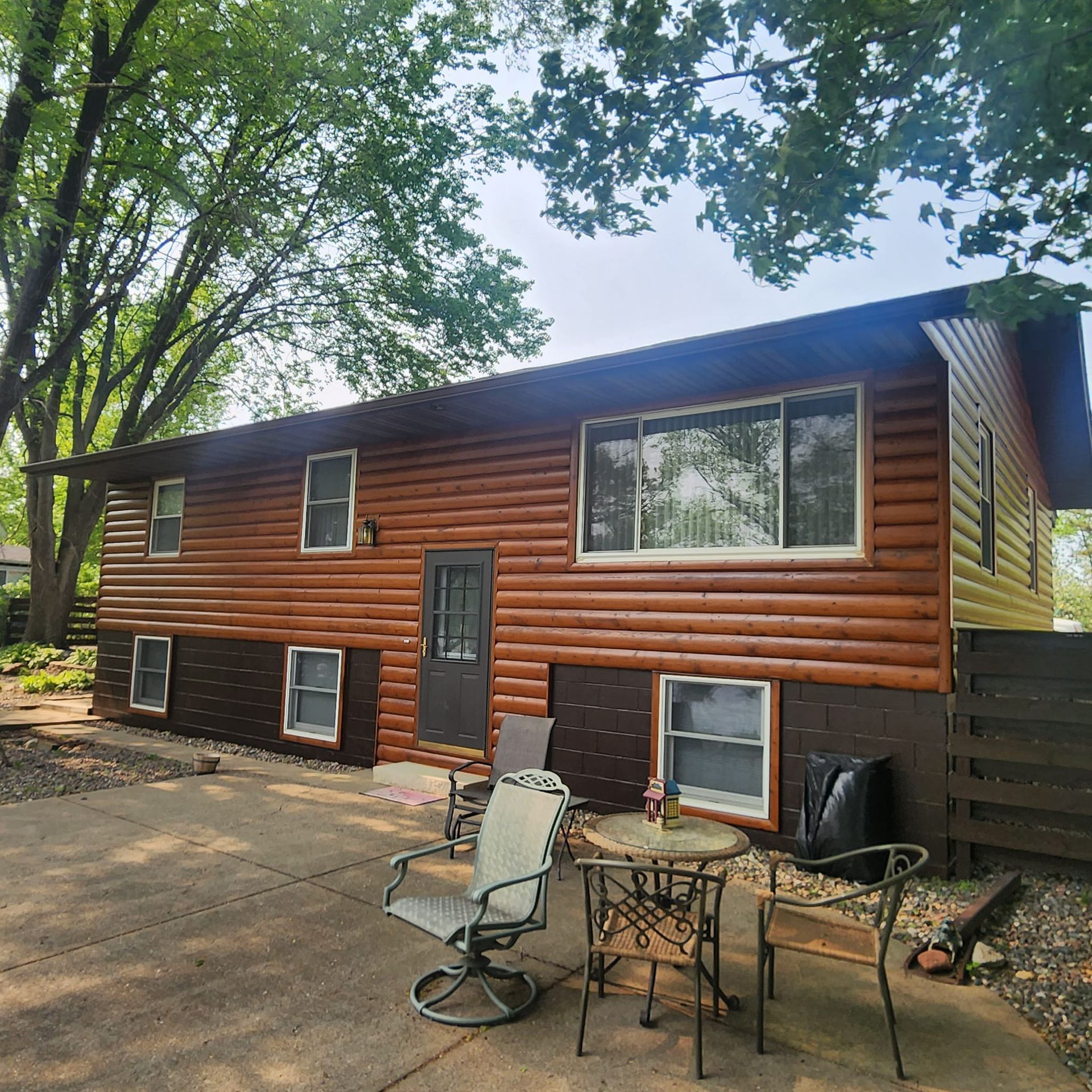 Brown cabin-style house with a patio, table, and chairs in front.