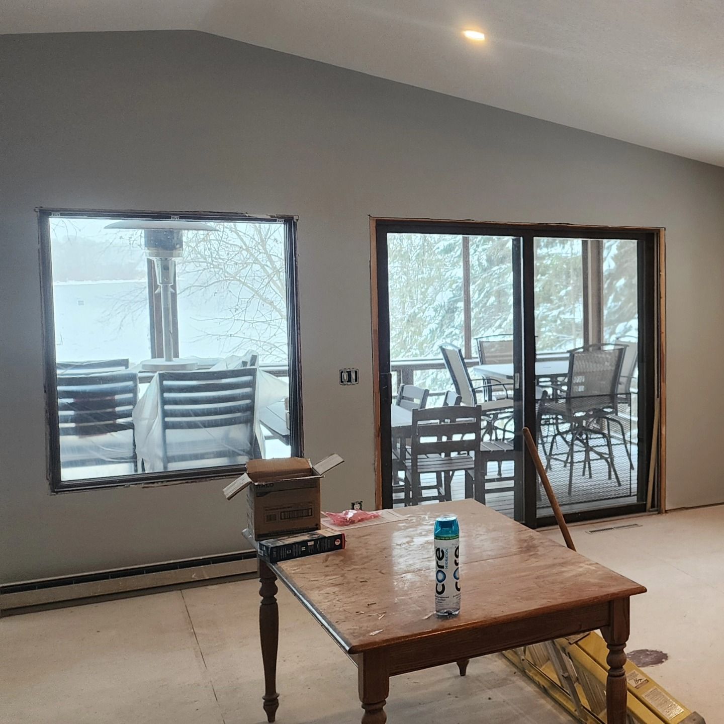Interior with a snowy view through a window and sliding glass door. A table and boxes are in the foreground.