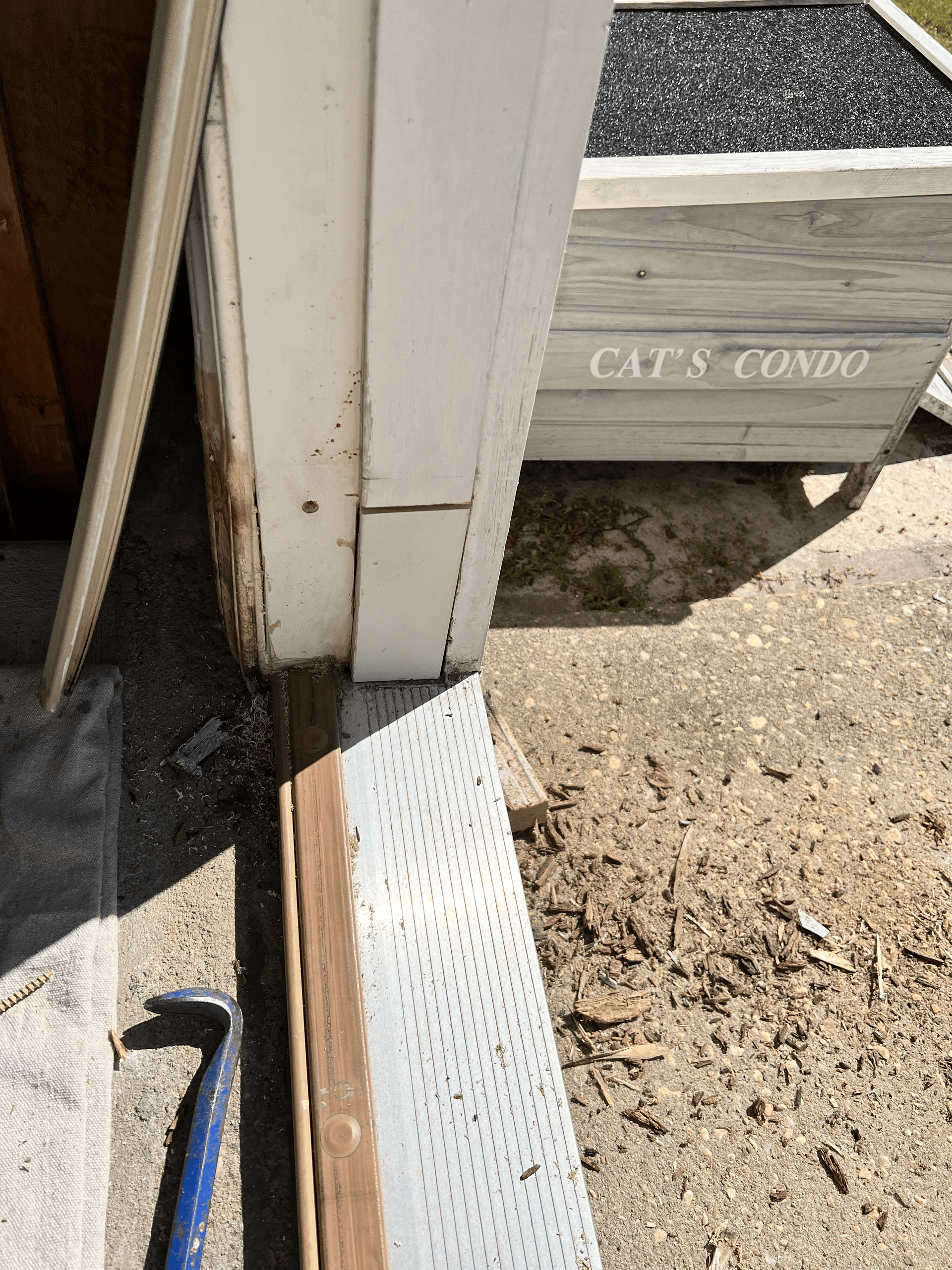 Exterior door frame with damaged trim and a planter labeled 