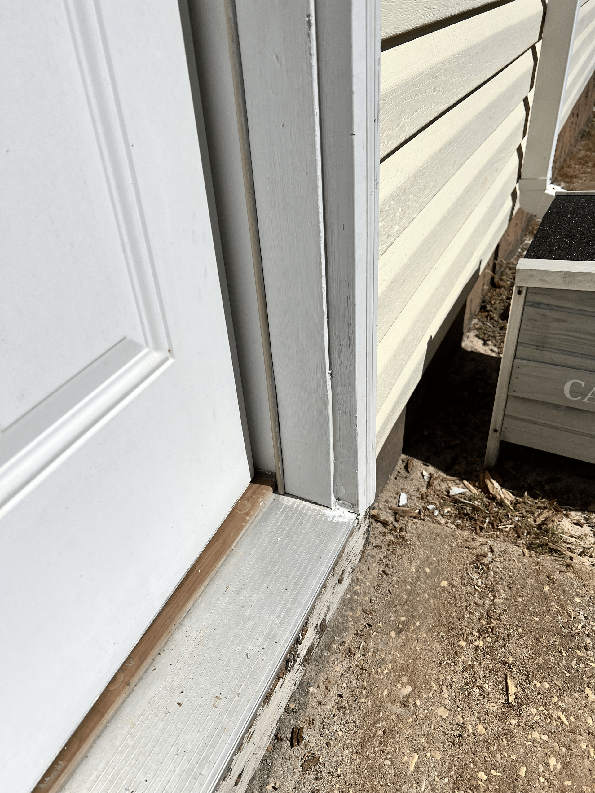 White door frame next to beige siding, with a concrete threshold on the ground.