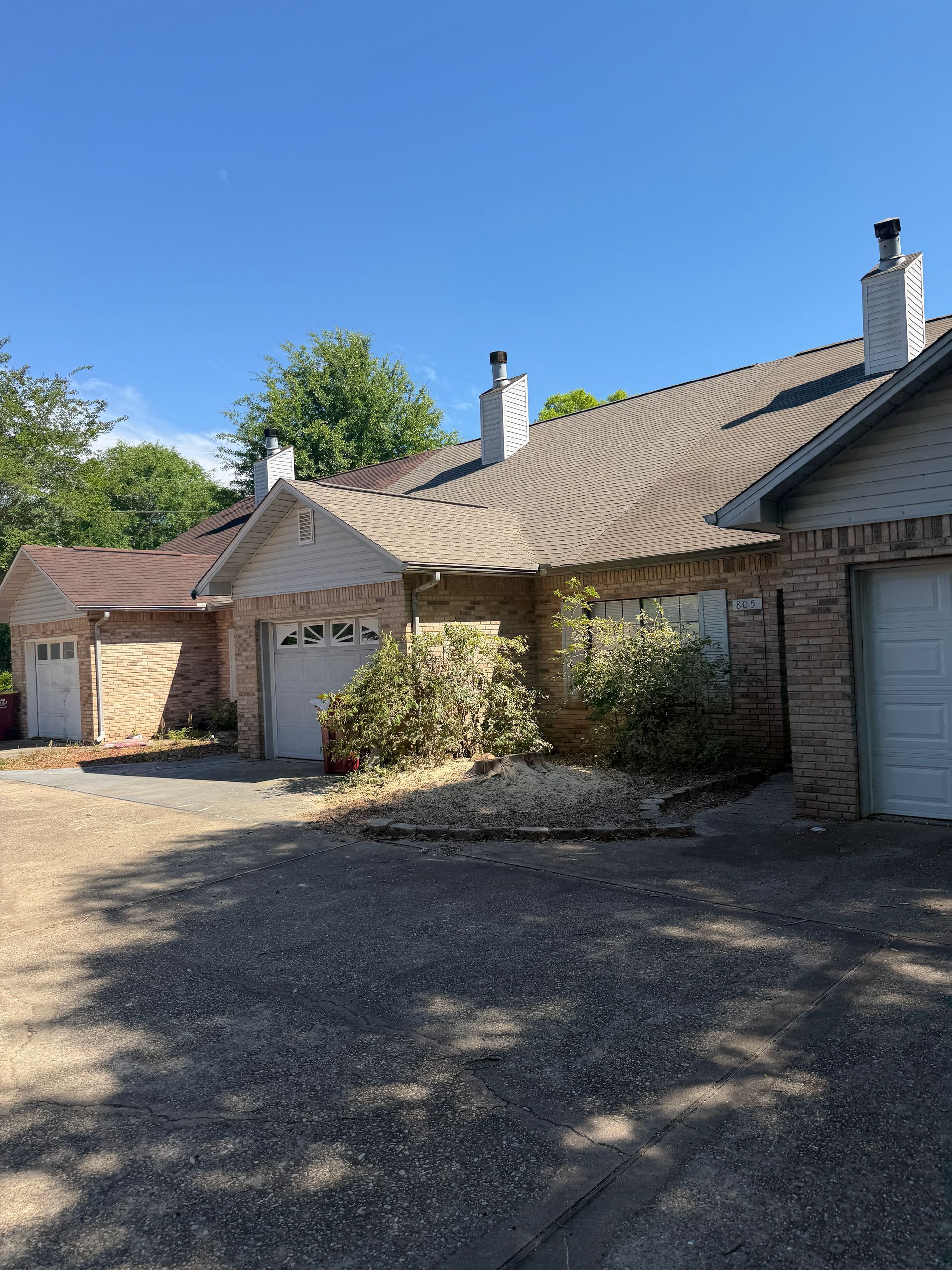 A single-story brick house with a yellow chimney and brown garage door on a sunny day.