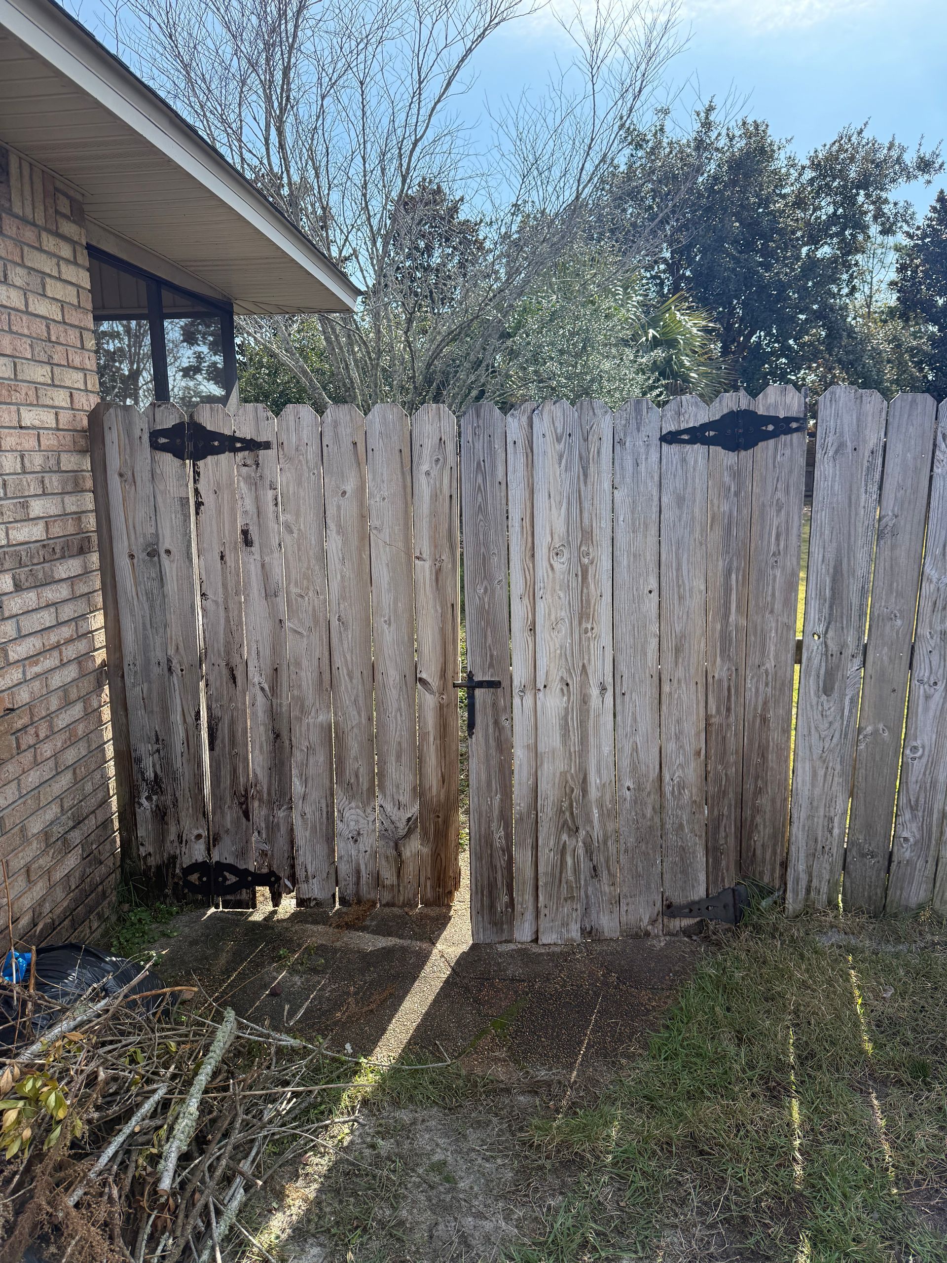 Weathered wooden fence with black hinges and latch, partially open, beside a brick building.