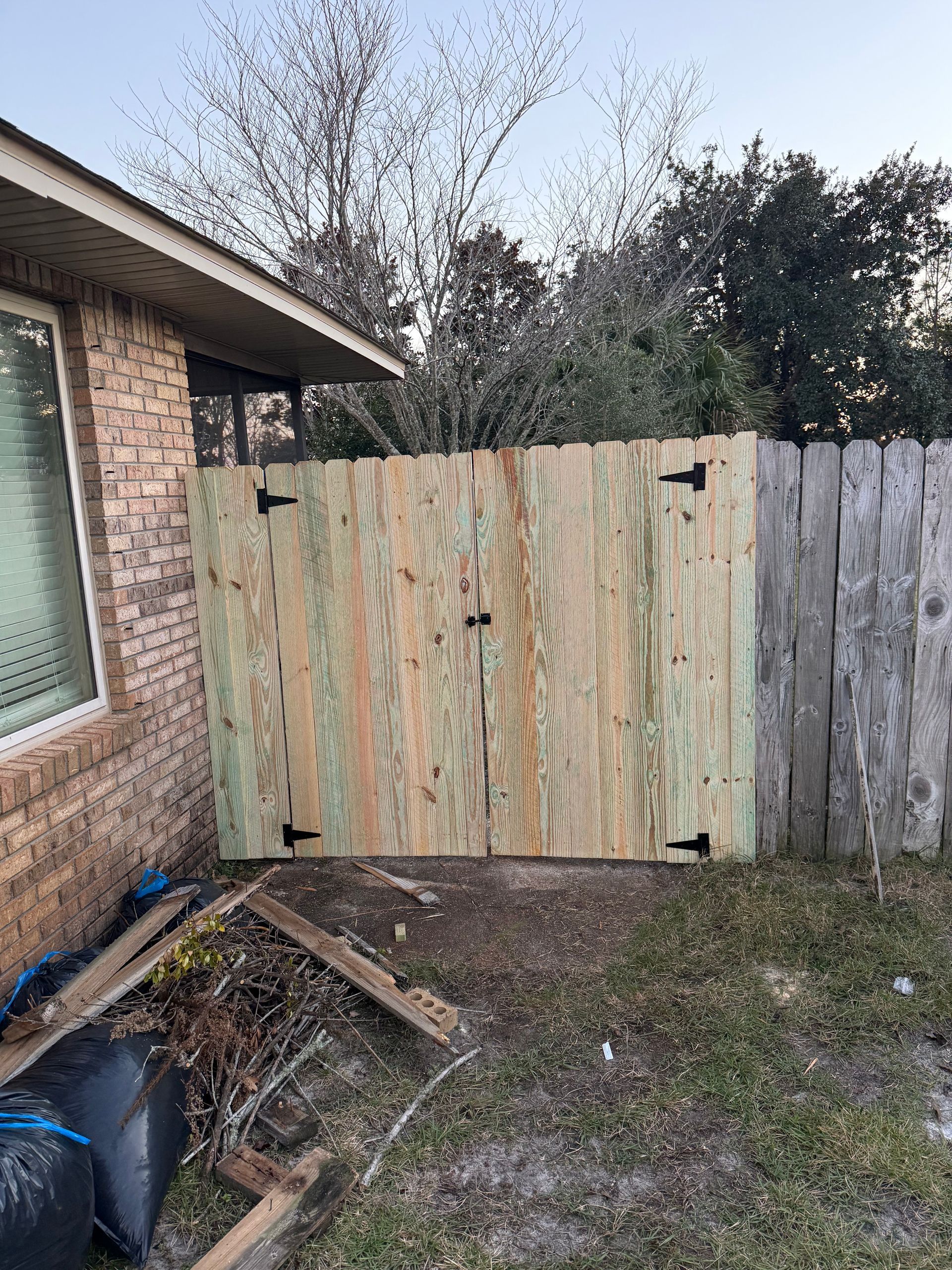 Wooden gate in a backyard, attached to a brick building and a wooden fence.