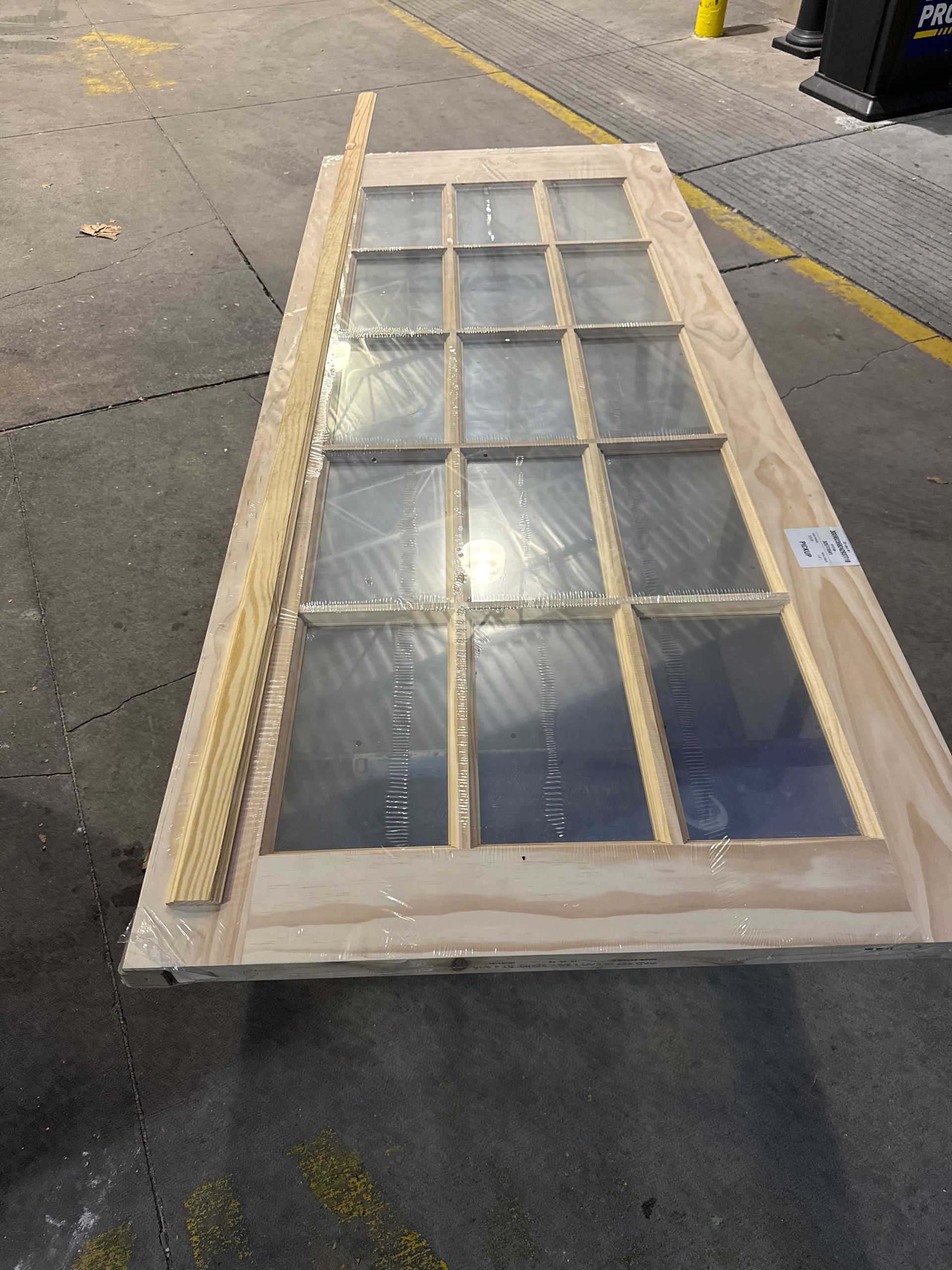 Wooden door with multiple glass panes, wrapped in plastic, lying on pavement.