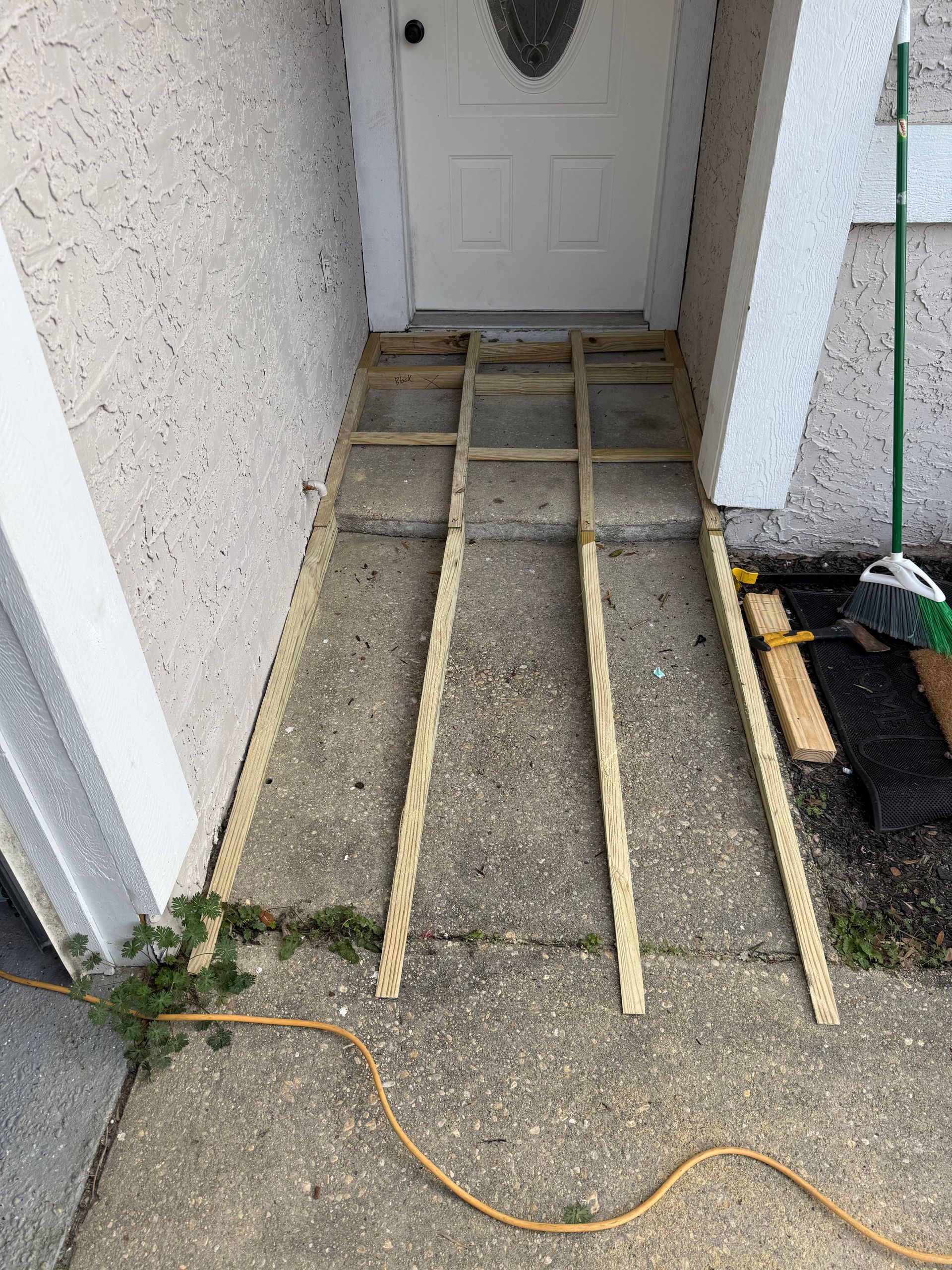 Wooden frame laid on concrete leading to a white door; possibly for a ramp.