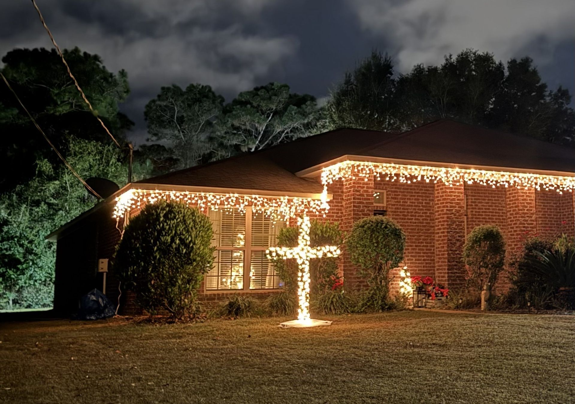 House with Christmas lights and a glowing cross on the lawn at night.