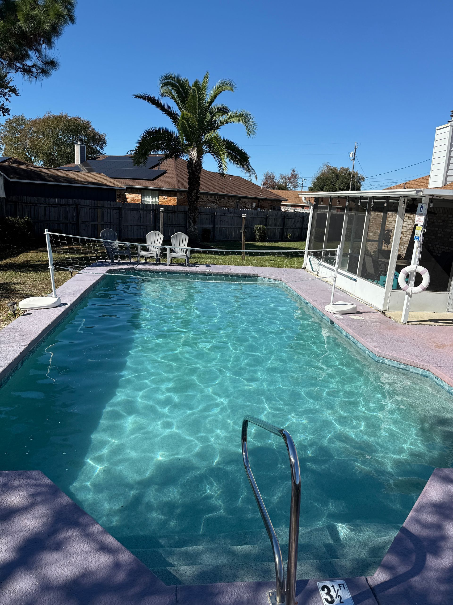 Swimming pool with turquoise water, stairs, and a palm tree under a bright blue sky.