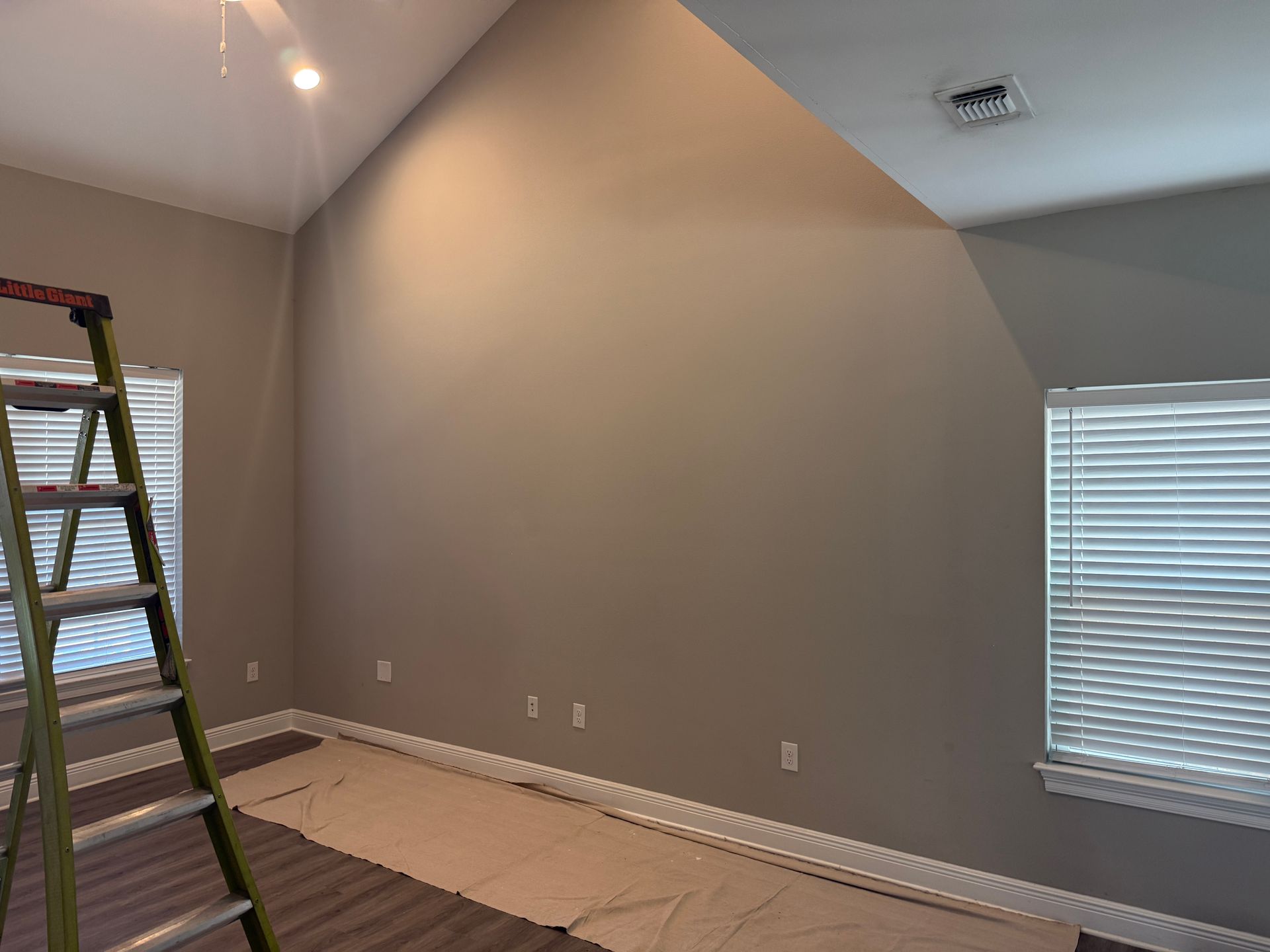 Interior of a room with tan walls, a high angled ceiling, windows, and a ladder.