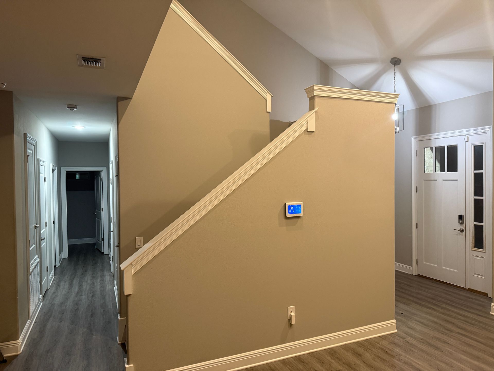 Hallway with staircase, tan walls, white trim, and a white front door.