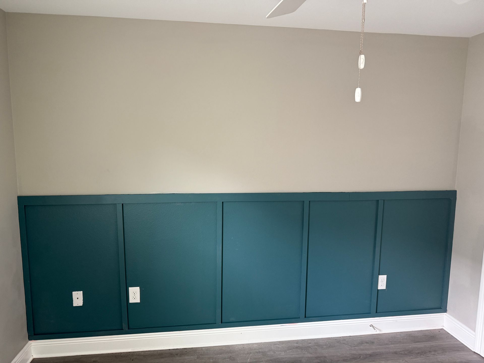 Teal cabinets across the bottom of a wall, cream paint above. White ceiling fan and light.