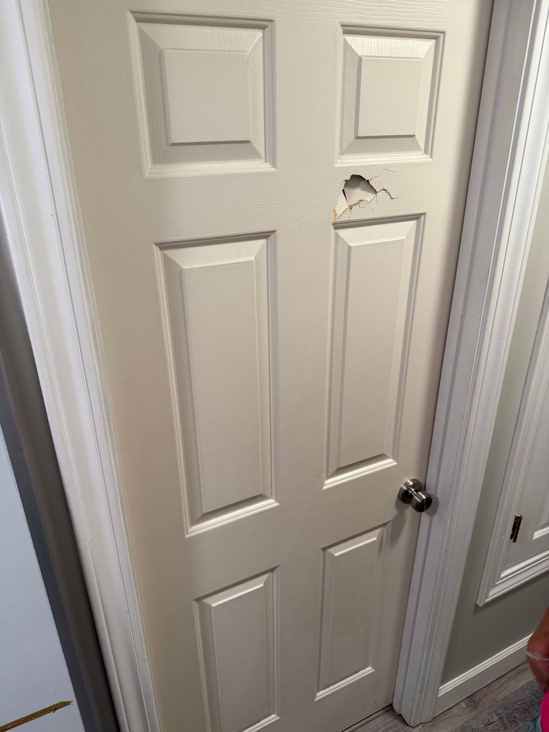 Cream-colored interior door with a hole, set in a white door frame.