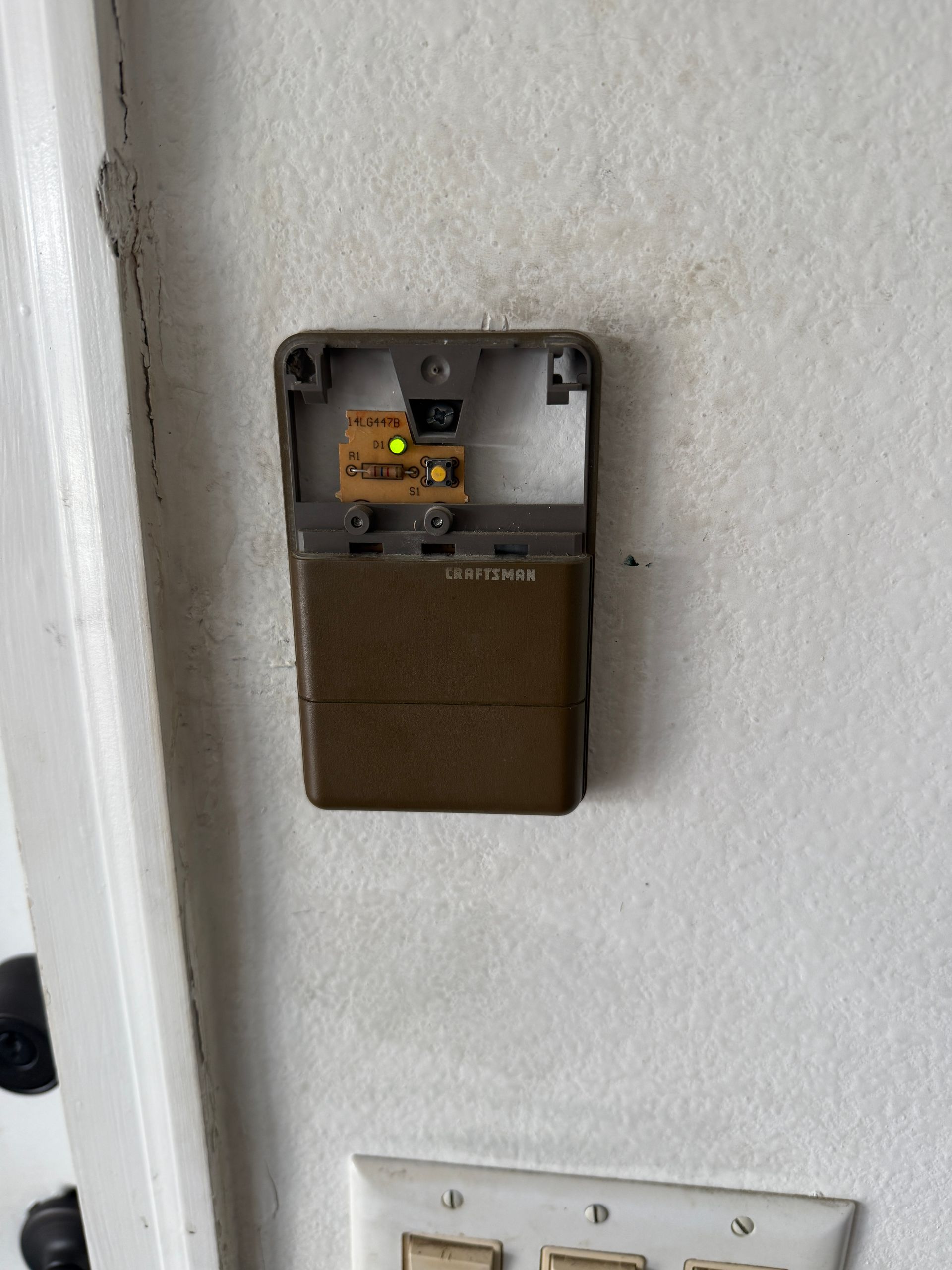 Brown doorbell on white wall, with visible circuitry and a yellow light illuminated.