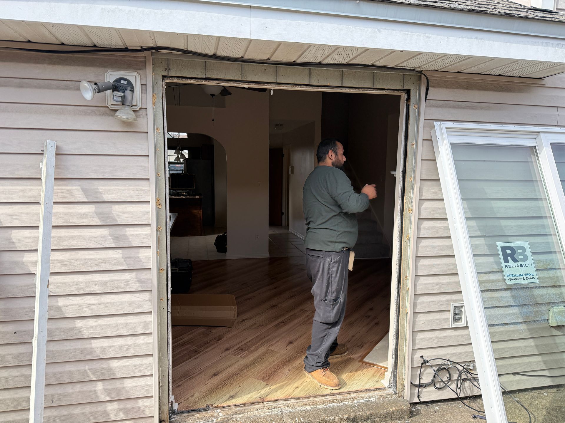 Man standing in doorway with new hardwood floor, preparing to install a sliding glass door.