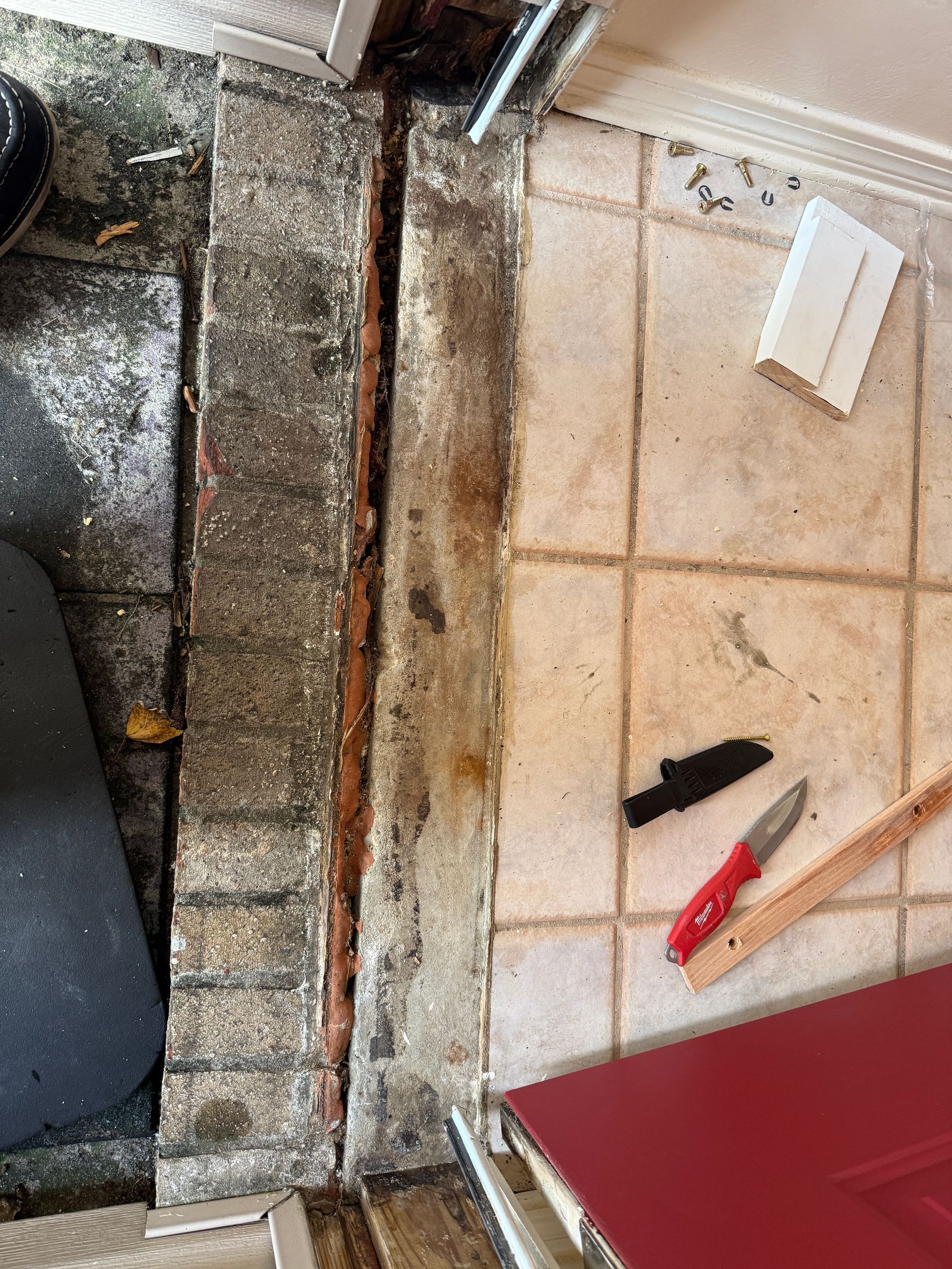 Gap in flooring exposes brick and wood, with tools and debris scattered.