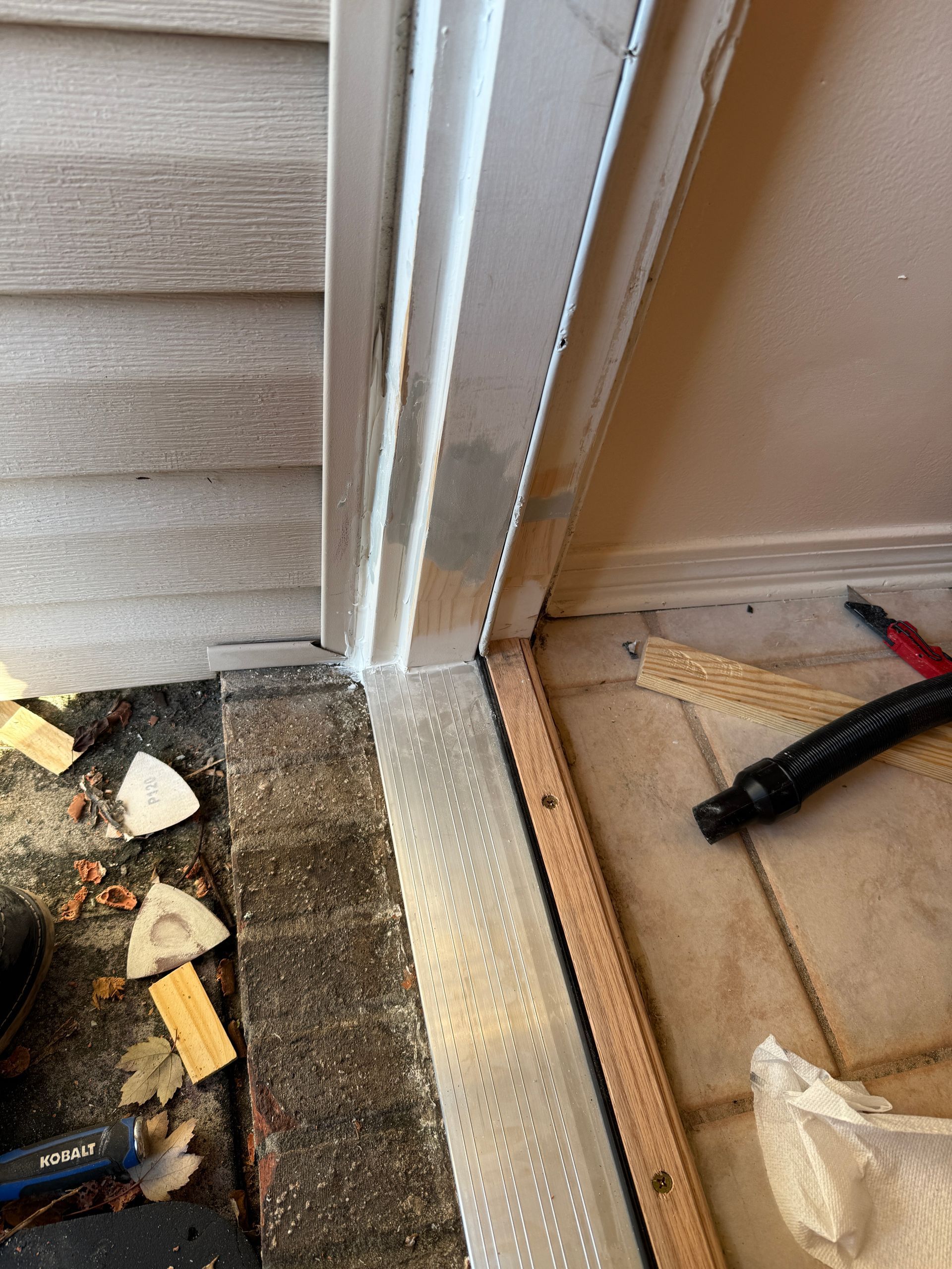 Door threshold showing damage and potential water infiltration; siding and interior flooring visible.