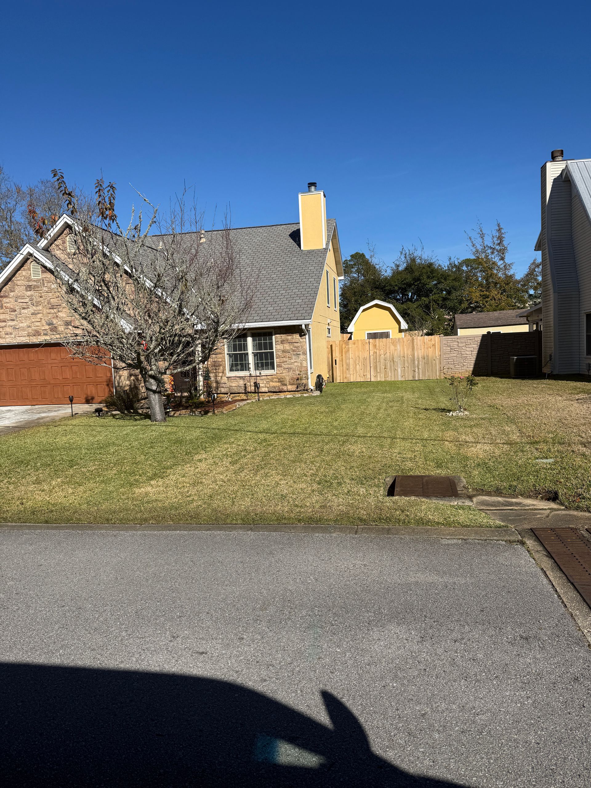A single-story brick house with a yellow chimney and brown garage door on a sunny day.