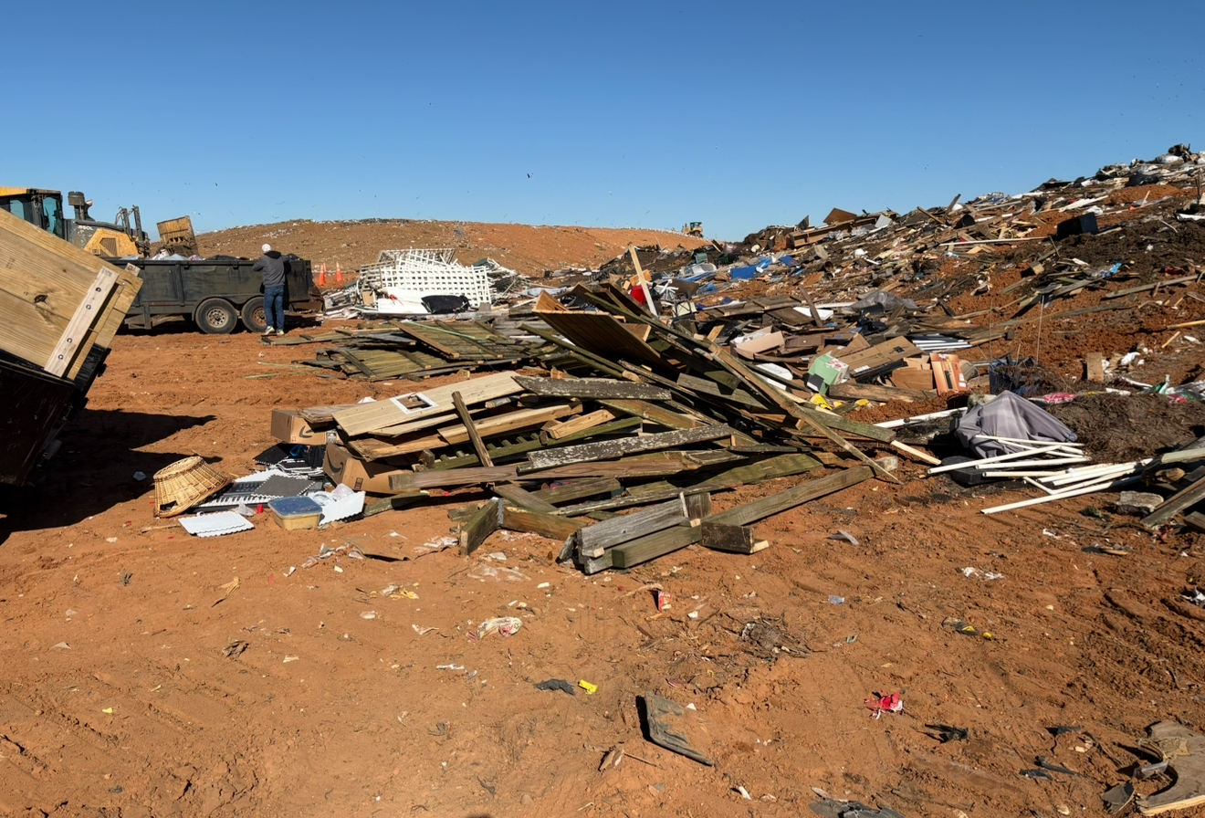 Landfill with dirt, trash, and heavy machinery, under a blue sky.