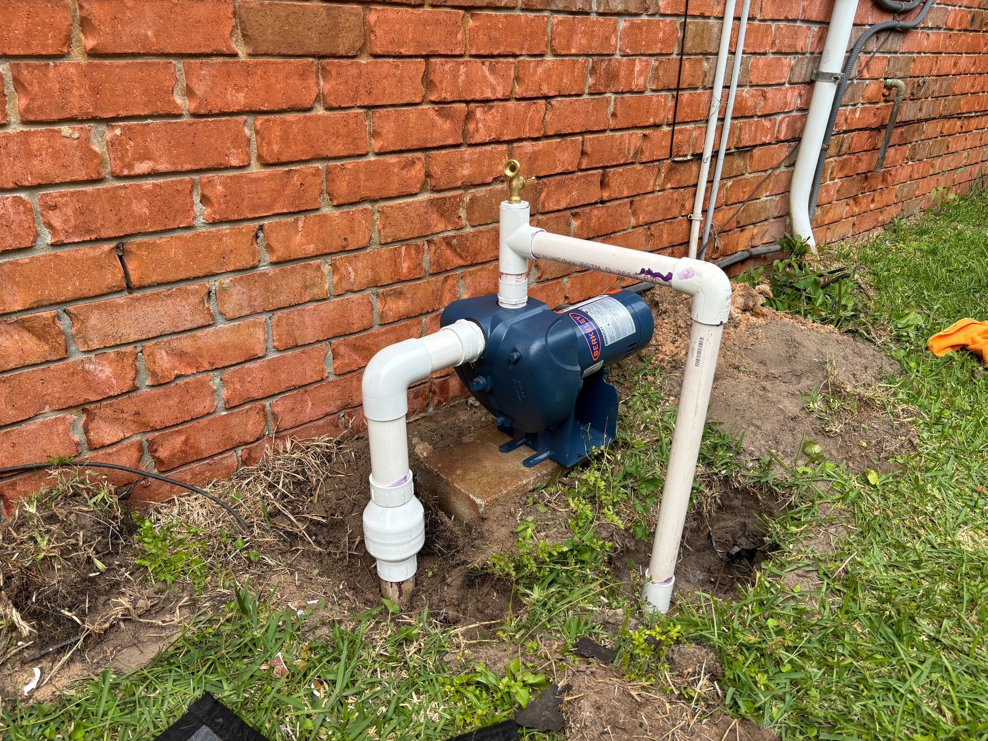 Blue water pump with white PVC pipes next to a brick wall.