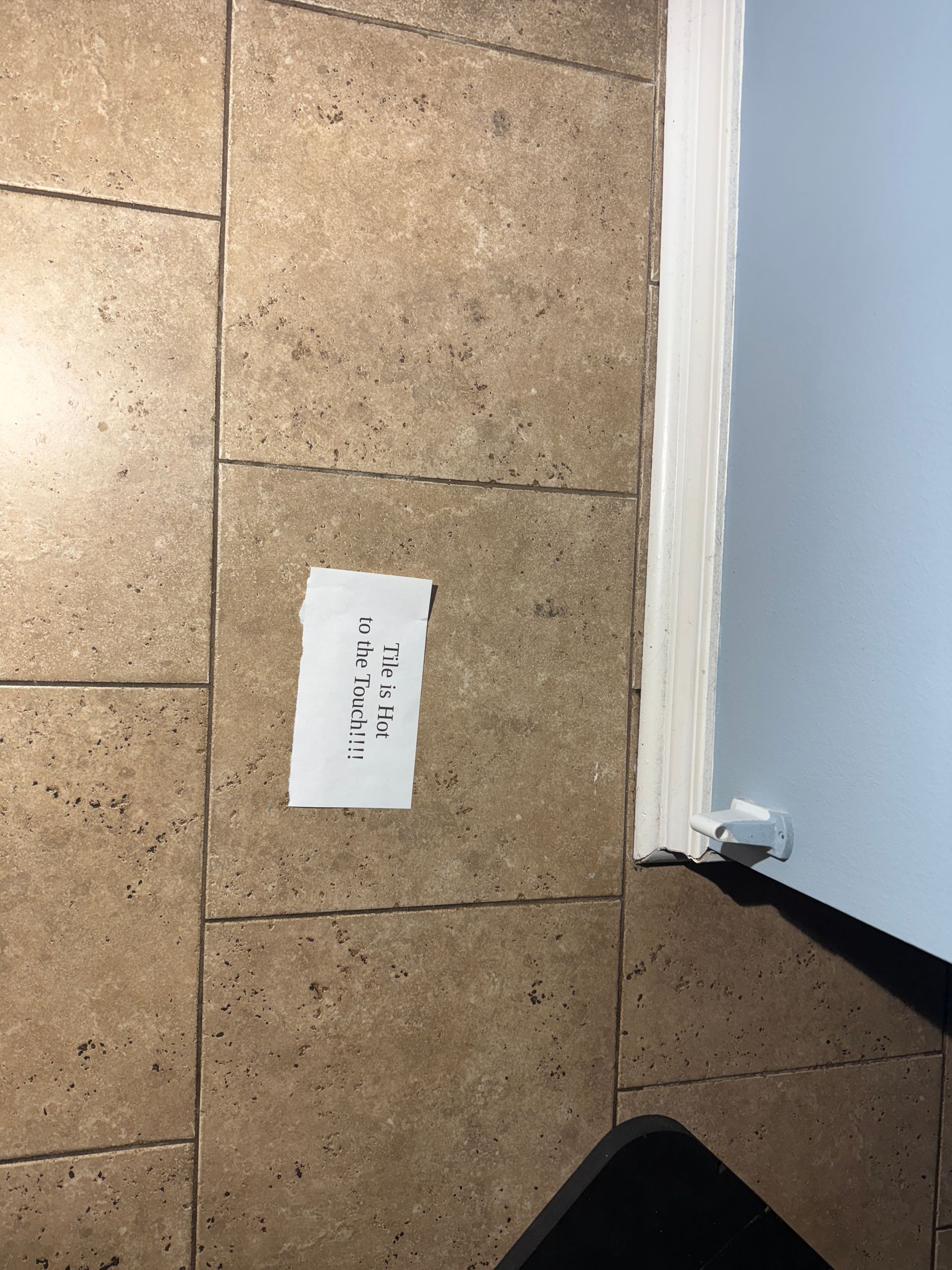 A torn paper note on a beige tiled floor next to a pale blue wall and white trim.