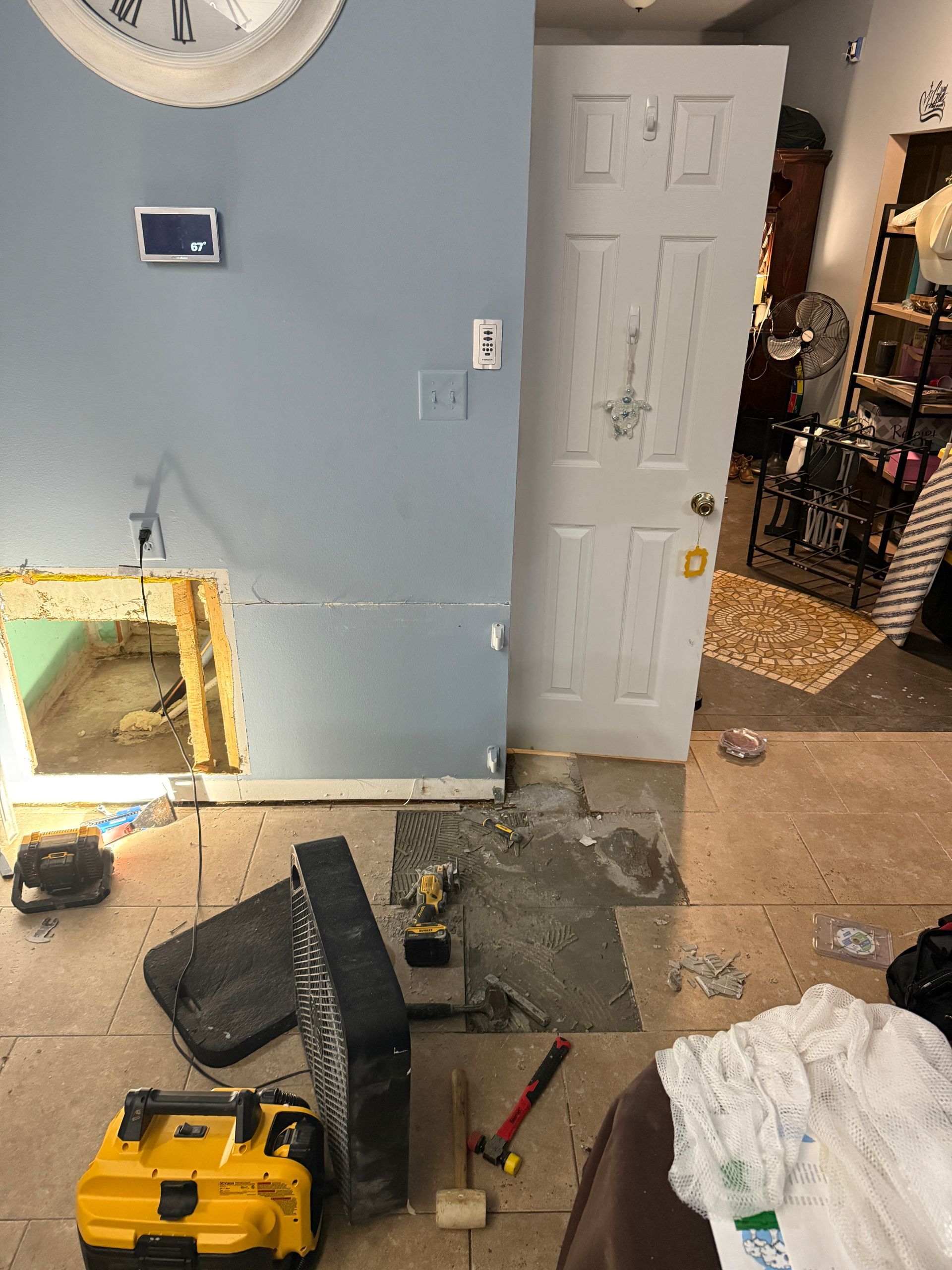Renovated interior: wall with open hole, doorway, and flooring under construction with tools.