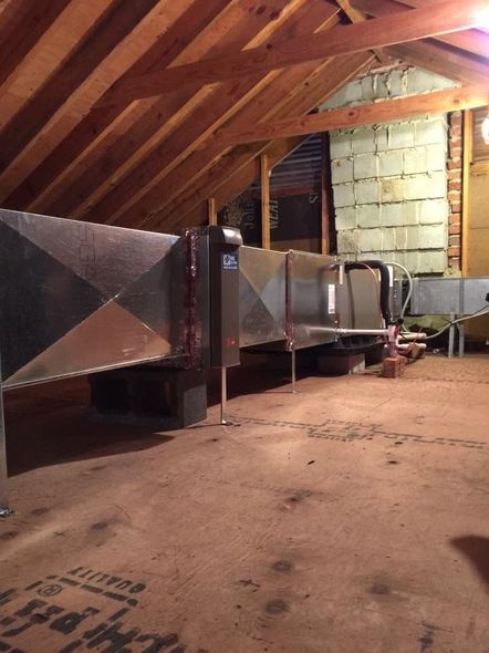 Attic with metal HVAC ductwork and insulation under a slanted wooden roof