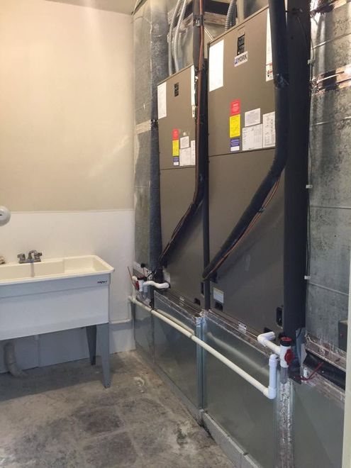 Basement utility room with two large HVAC units, exposed piping, and a small utility sink.